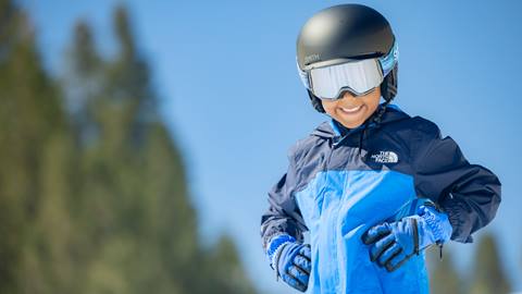 Young child wearing blue colored snow gear smiling at the camera